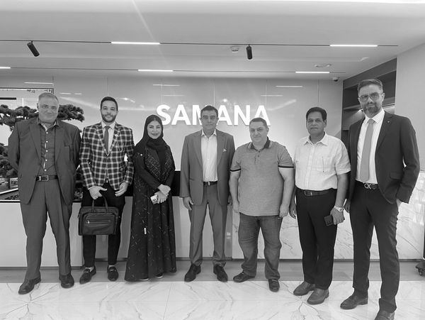 Group of seven professionals posing together indoors in front of a wall with the word SAMANA.
