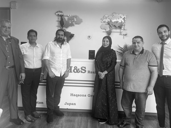 Group of six people posing in an office setting with a company sign behind them.